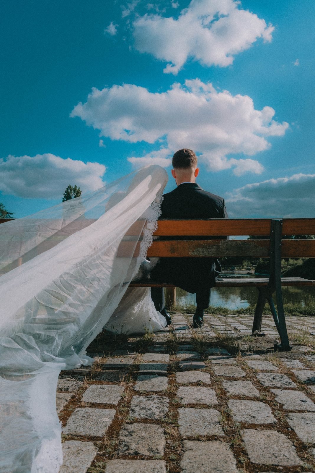 Le voile de la mariée au vent, le marié assis sur un banc